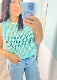 Woman taking a mirror selfie wearing a  mint green sleeveless crochet top  and jeans.
