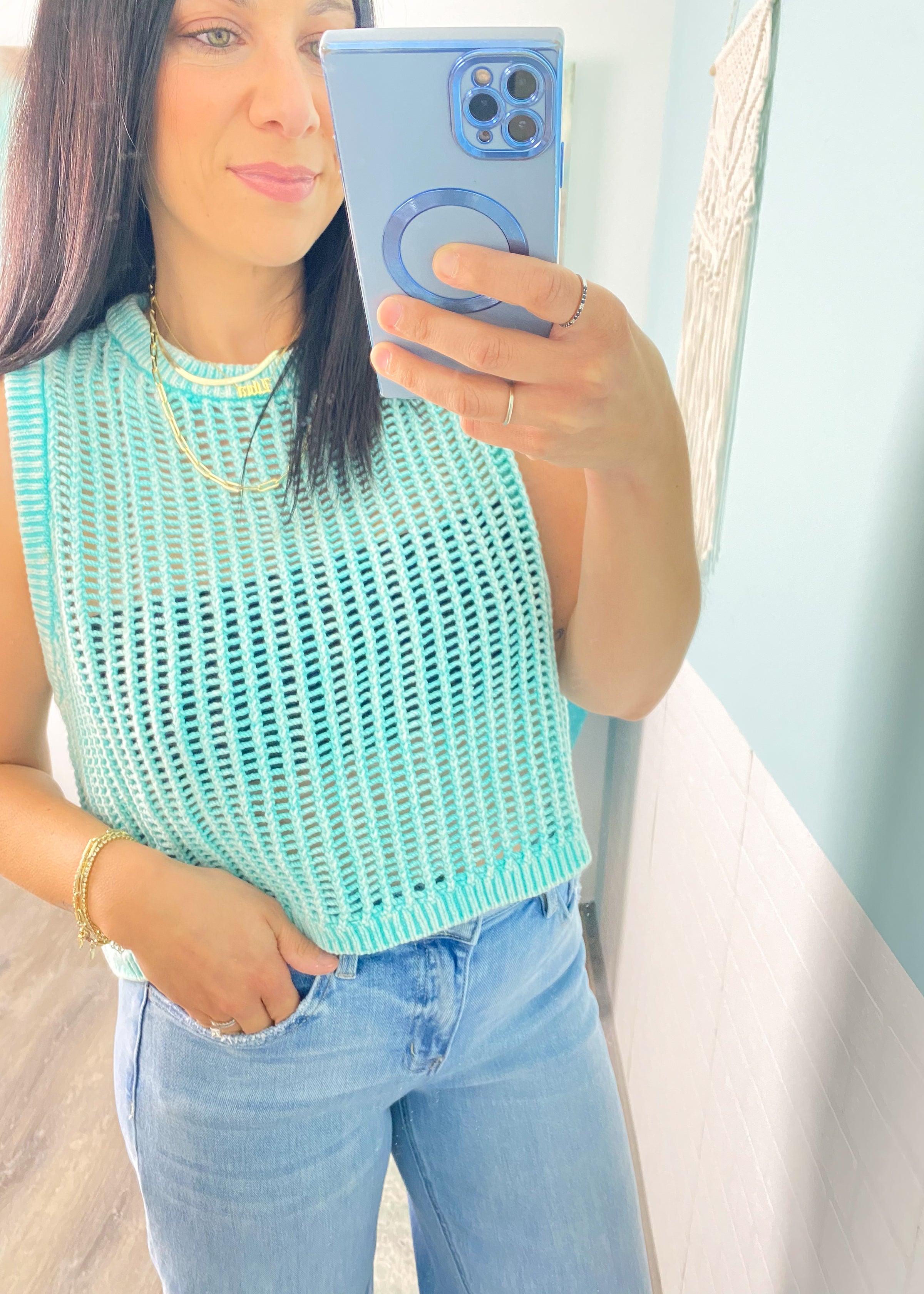 Woman taking a mirror selfie wearing a  mint green sleeveless crochet top  and jeans.