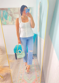 Woman taking a mirror selfie wearing a white peplum top and blue jeans, holding a green handbag.