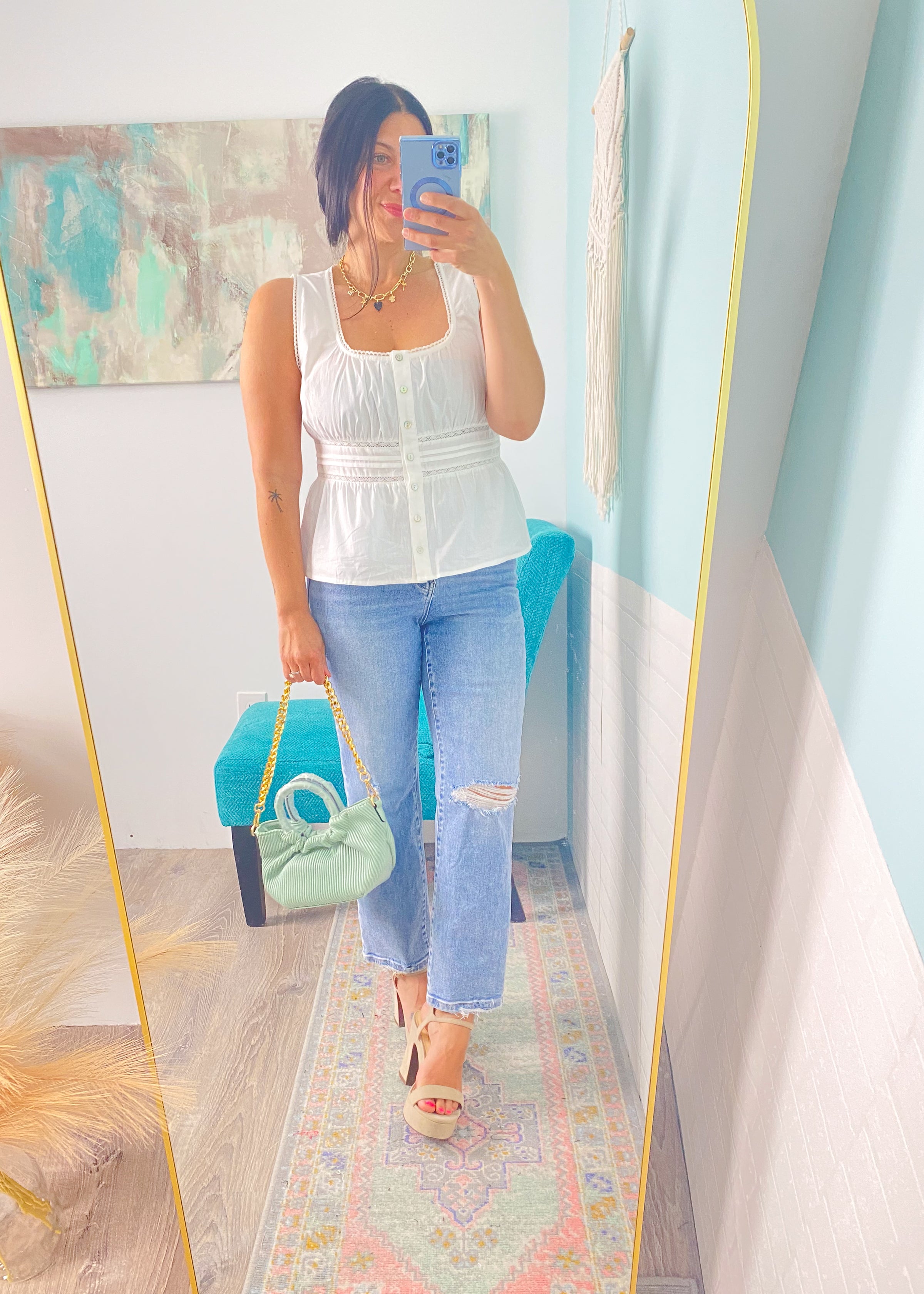 Woman taking a mirror selfie wearing a white peplum top and blue jeans, holding a green handbag.