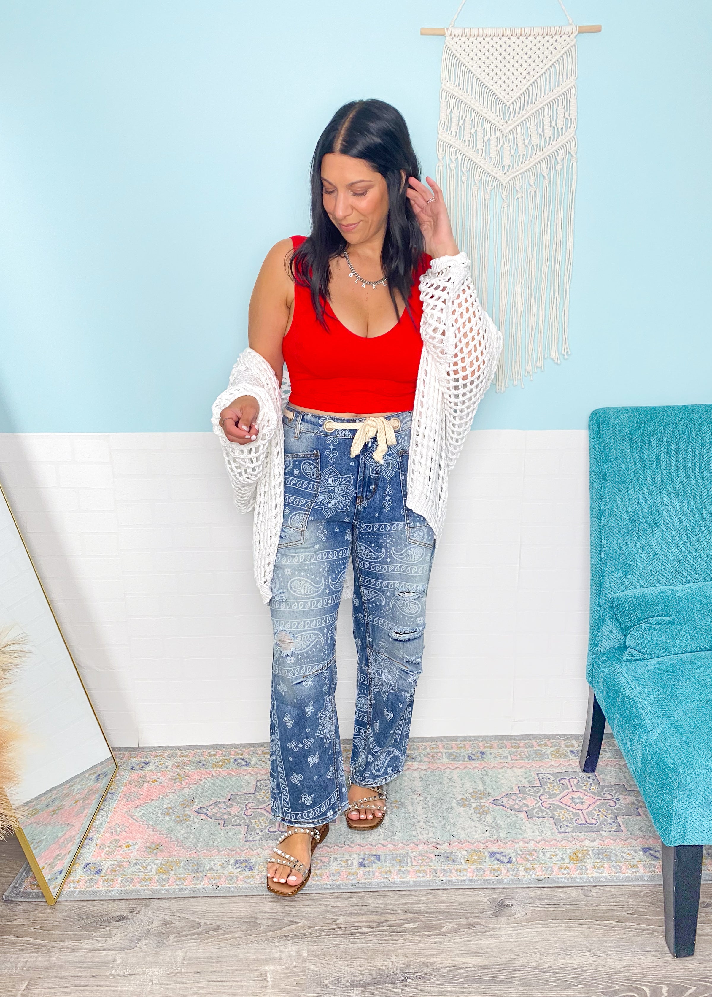 Woman wearing a red lace patterned seamless cropped top and blue paisley jeans in a room with a white wall and a blue chair.