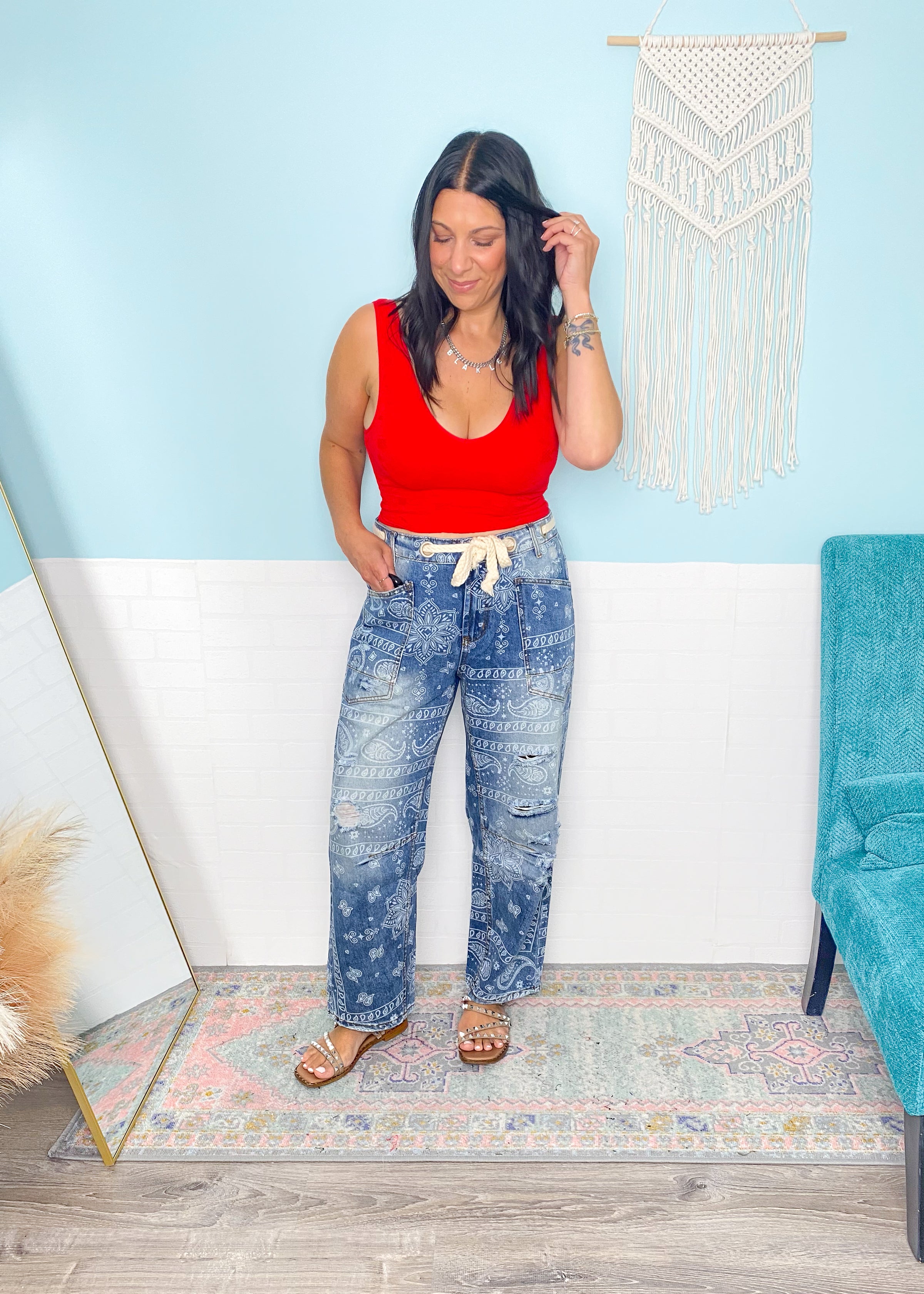 Woman in a red lace patterned seamless cropped top and blue jeans standing in a room with a white wall and decorative elements.