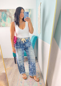 Woman taking a mirror selfie wearing a white lace patterned seamless cropped top and blue paisley printe pants in a room with colorful decor.