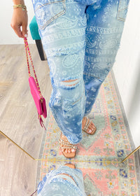 Person wearing light blue paisley printed jeans on a wooden floor with a colorful rug.