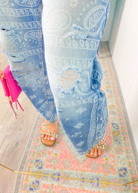Person wearing light blue jeans with a paisley pattern on a colorful rug.