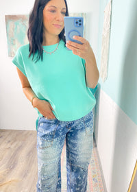 Woman taking a mirror selfie wearing a mint green top and light blue paisley printed jeans.