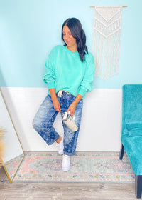 Woman in mint green sweatshirt and jeans standing in a room with a blue wall and decorative rug.