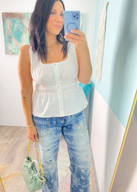 Woman taking a mirror selfie wearing a white peplum top and blue paisley patterned jeans, holding a green handbag.