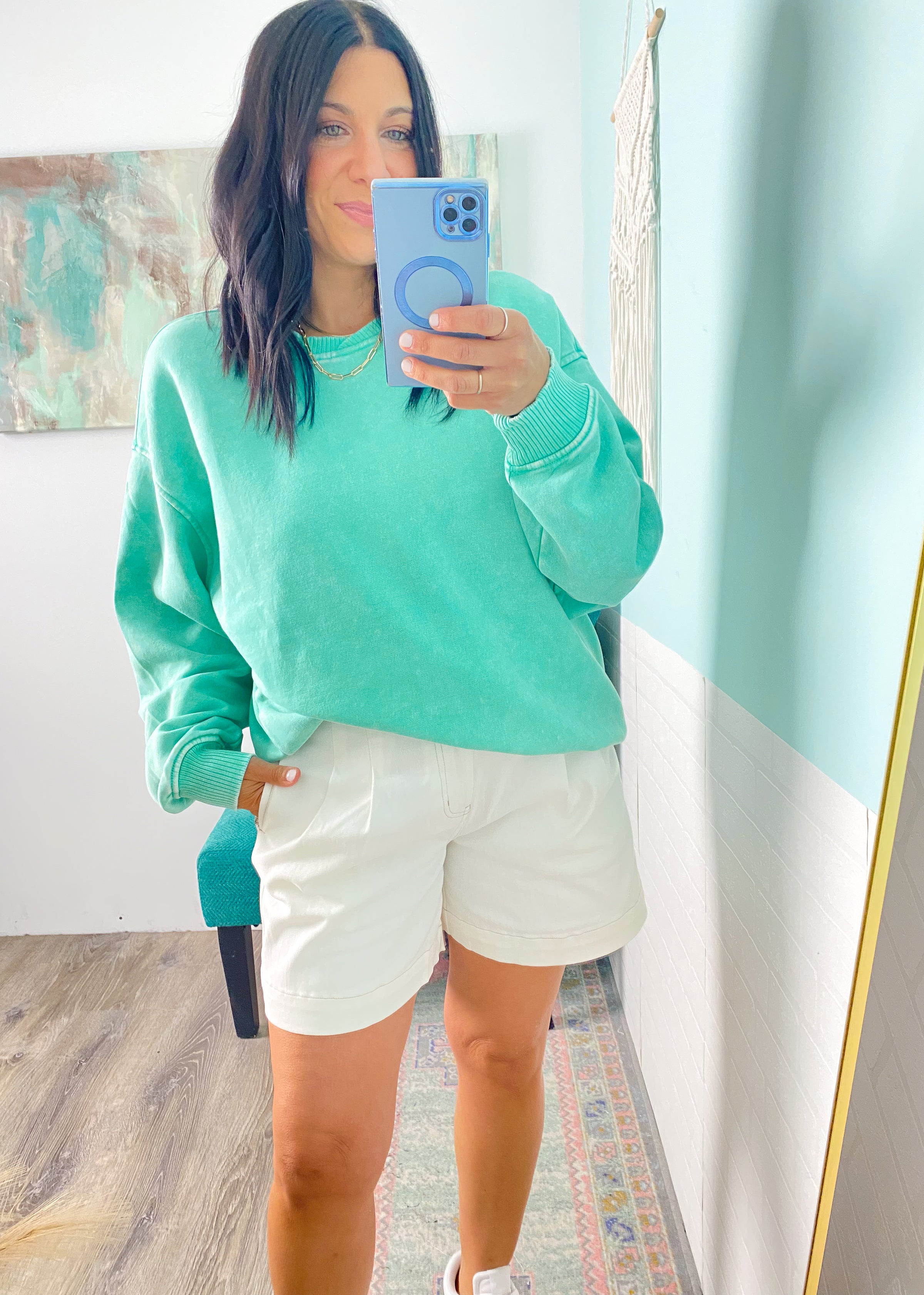 Person wearing a teal sweatshirt and white shorts taking a mirror selfie.