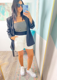 Woman taking a mirror selfie wearing a striped top, white shorts, and a dark blazer.