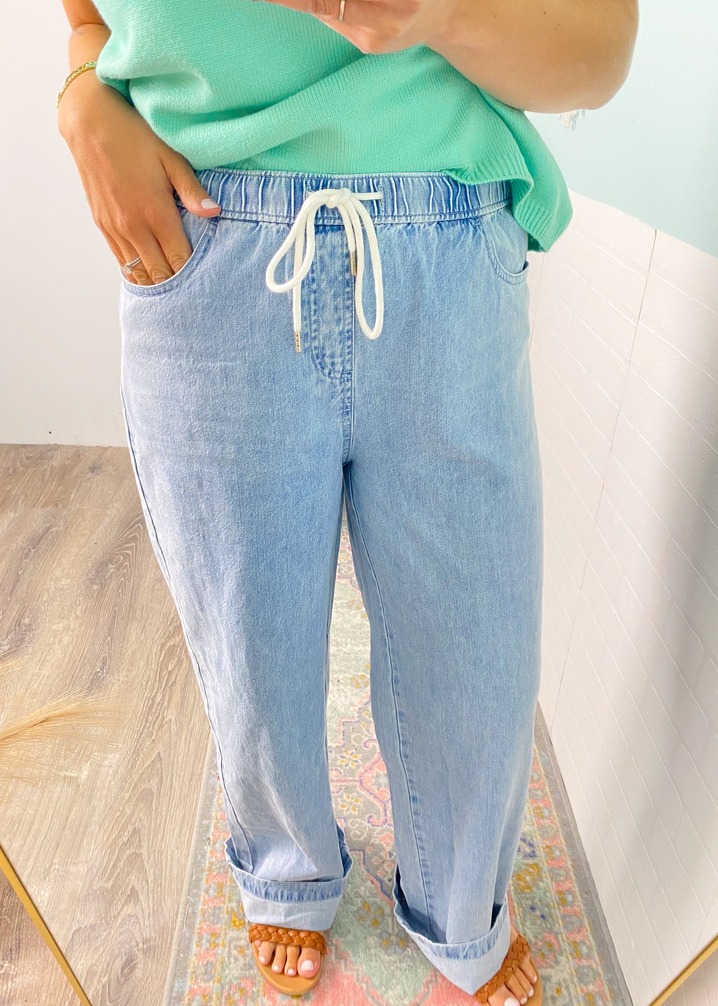 Person wearing light blue jeans and a green top on a neutral background