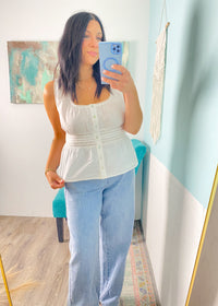 Woman taking a mirror selfie wearing a white peplum top and blue jeans in a room with a colorful rug and map on the wall.