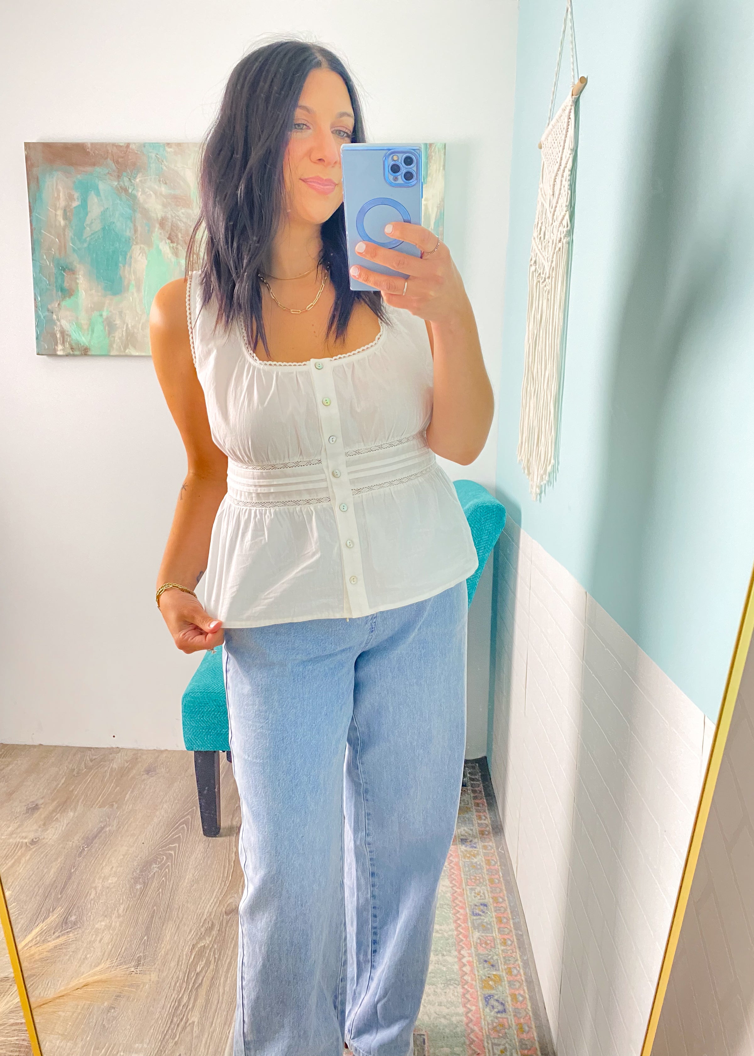 Woman taking a mirror selfie wearing a white peplum top and blue jeans in a room with a colorful rug and map on the wall.