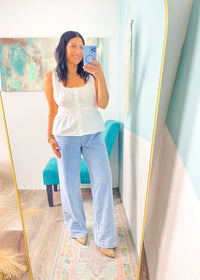 Woman taking a mirror selfie wearing a white peplum top and light blue jeans in a room with a colorful rug and teal chair.