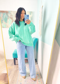 Person taking a mirror selfie wearing a green sweater and light blue jeans.