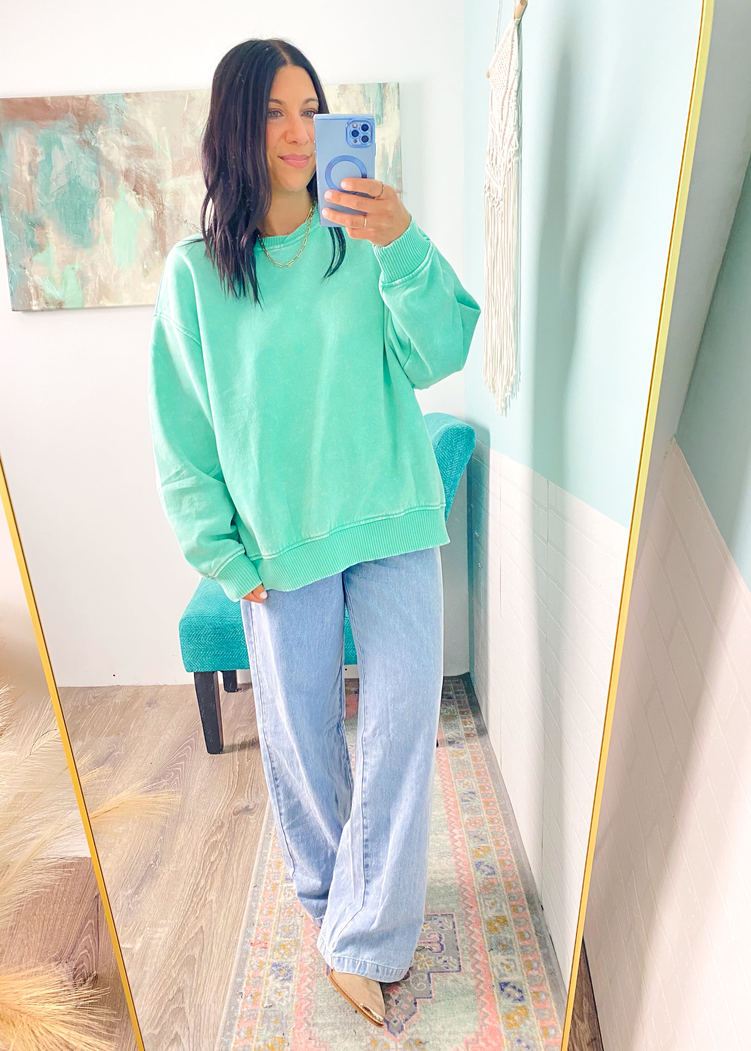 Person wearing a light green sweatshirt and light blue jeans taking a mirror selfie.