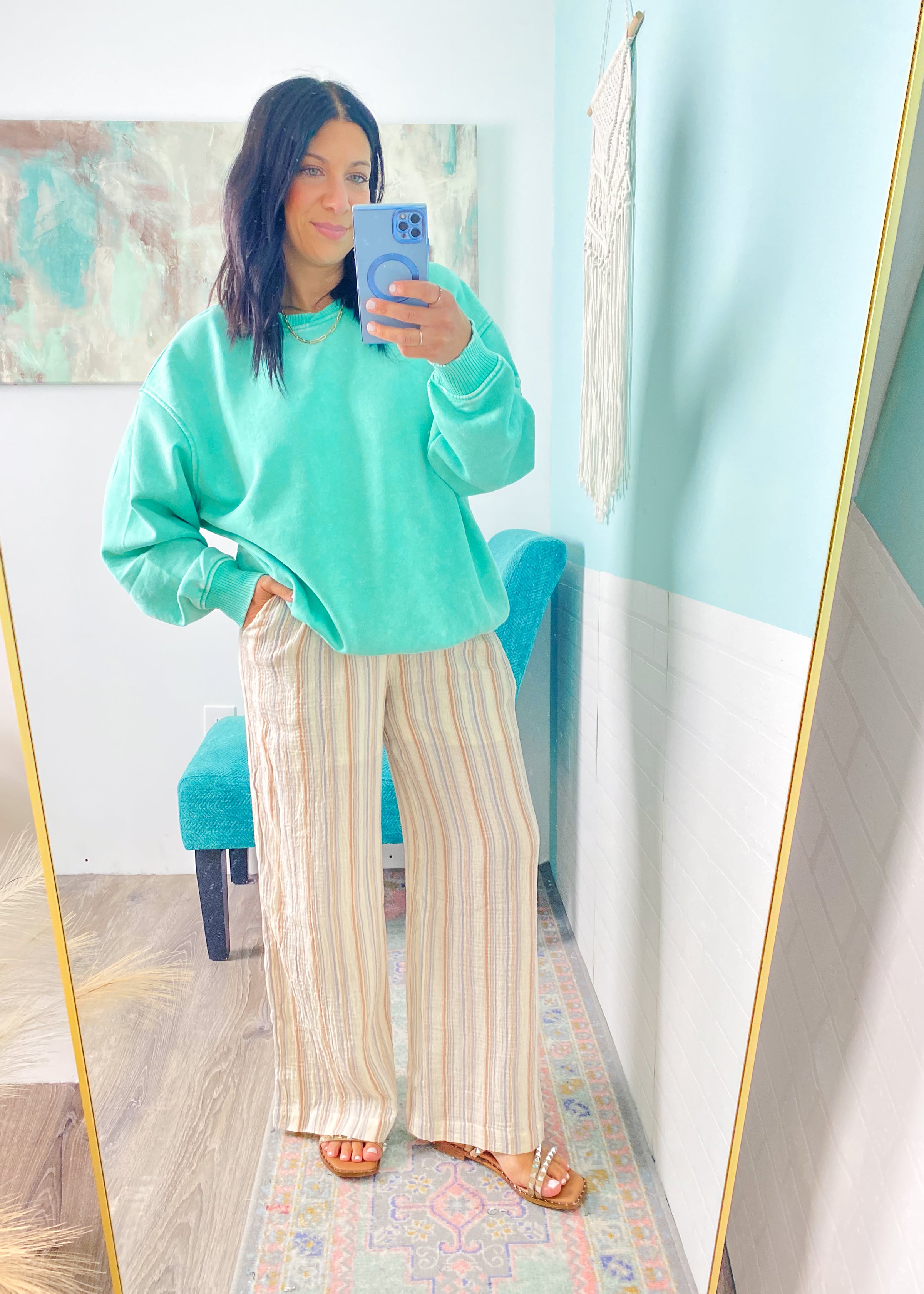 Person wearing a mint green sweatshirt and striped pants taking a mirror selfie.