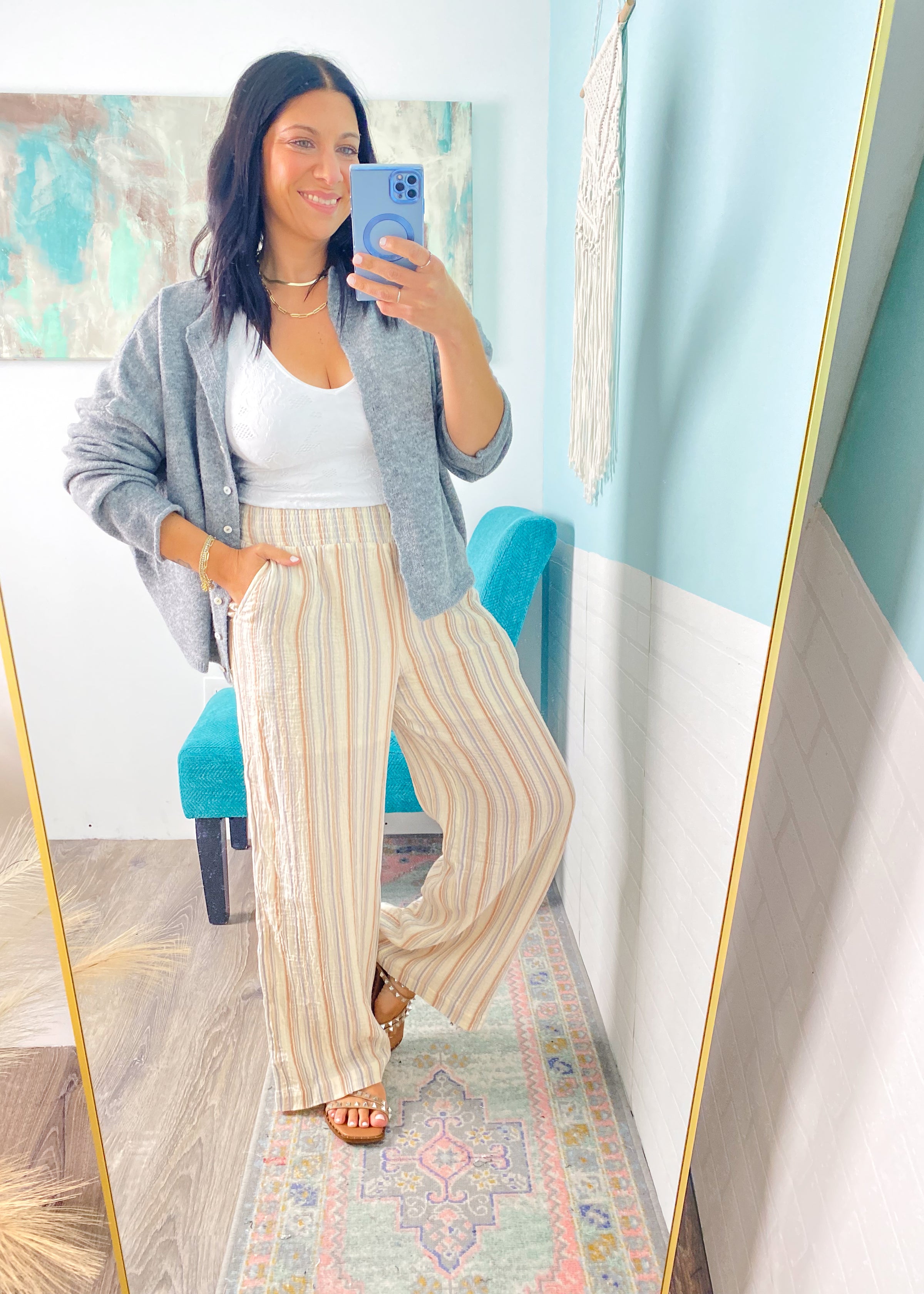 Woman taking a mirror selfie wearing a gray cardigan, white top, and striped pants.