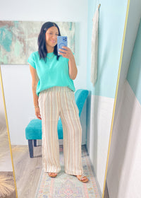 Woman taking a mirror selfie wearing a teal top and striped pants in a room with a blue wall.