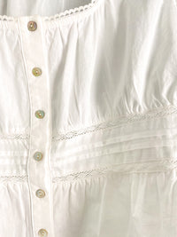 Close-up of a white peplum blouse with lace details and button details.