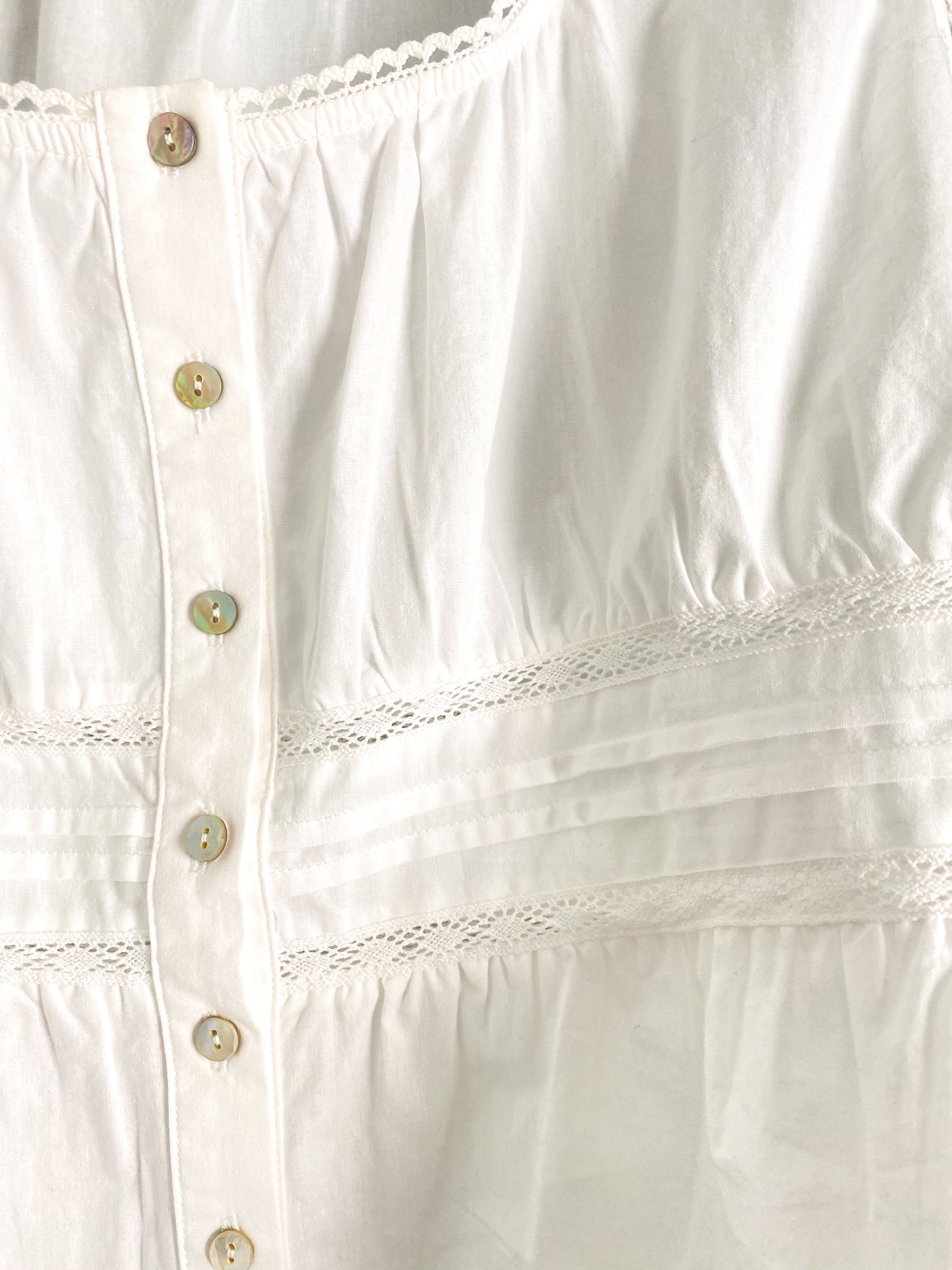 Close-up of a white peplum blouse with lace details and button details.
