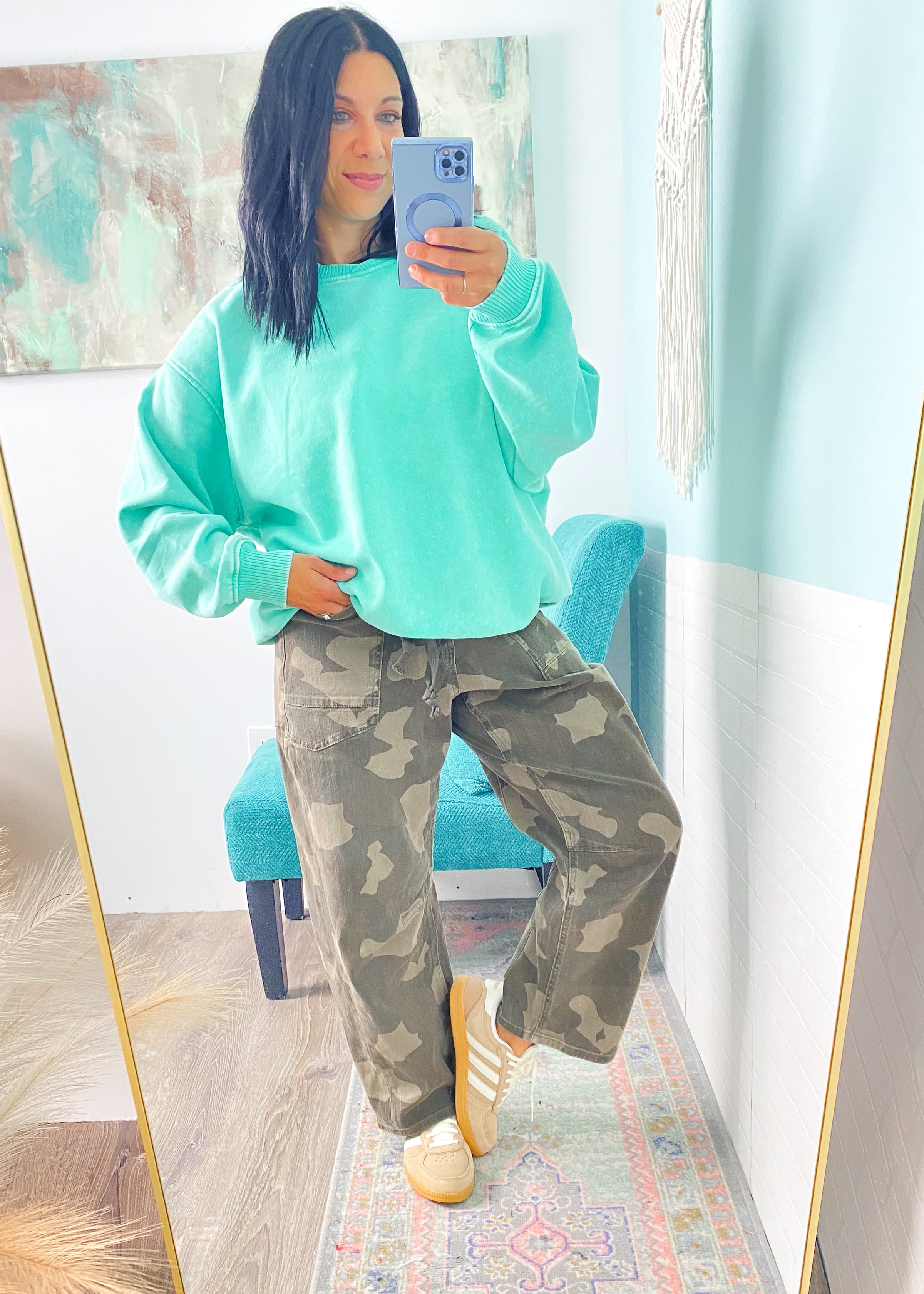 Person wearing a mint green sweatshirt and camouflage pants taking a mirror selfie.